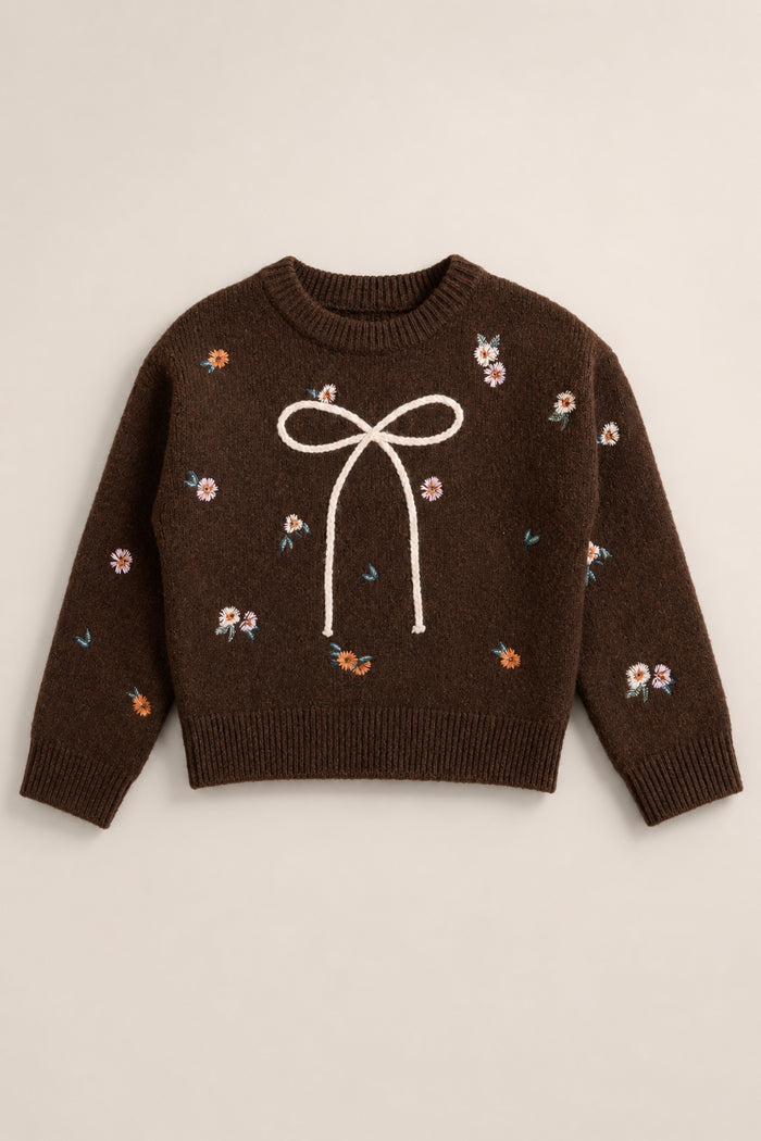 The Mini Ellis Sweater in Warm Cocoa Lovelorn Ditsy by Ivy City Co is a brown knit sweater featuring a large white bow design on the front, accented with embroidered multicolored ditsy flowers.
