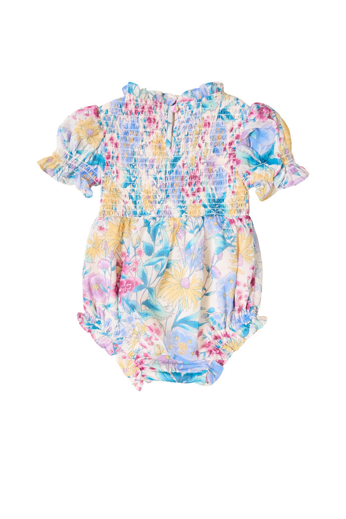 The Ivy City Co Baby Cordelia Romper in Pretty Plumeria showcases puffed short sleeves, a smocked top, and a floral pattern in pastel blue, pink, and yellow tones on a white background. This charming spring romper is perfect for any occasion.