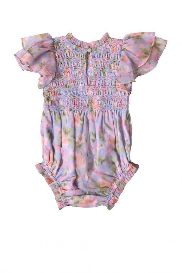 The Ivy City Co Baby Lottie Romper in Vibrant English Garden features ruffled flutter sleeves, a smocked bodice, gathered leg openings, and a pastel floral print with pink, purple, green, and yellow tones.