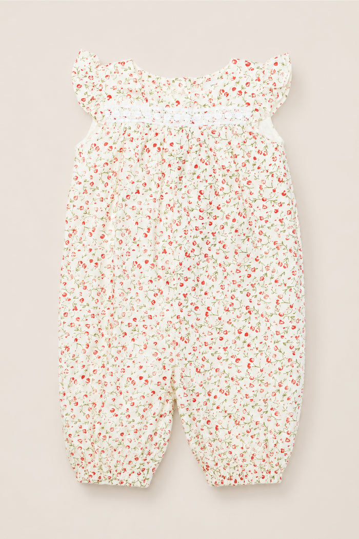The Ivy City Co Baby Mirabelle Romper in Cream Ditsy Floral features short ruffle sleeves, a gathered neckline, and a white background adorned with a delicate red and green floral print. Crafted from soft cotton, this charming romper is finished with lace trim for an extra touch of sweetness.