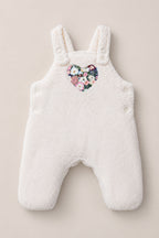 The Baby Siena Onesie in Ivory & Midnight Garden by Ivy City Co is a white fleece baby romper with shoulder straps and side buttons, adorned with a heart-shaped floral patch on the chest—an irresistibly cozy sleeveless piece that will keep your little one warm and stylish.
