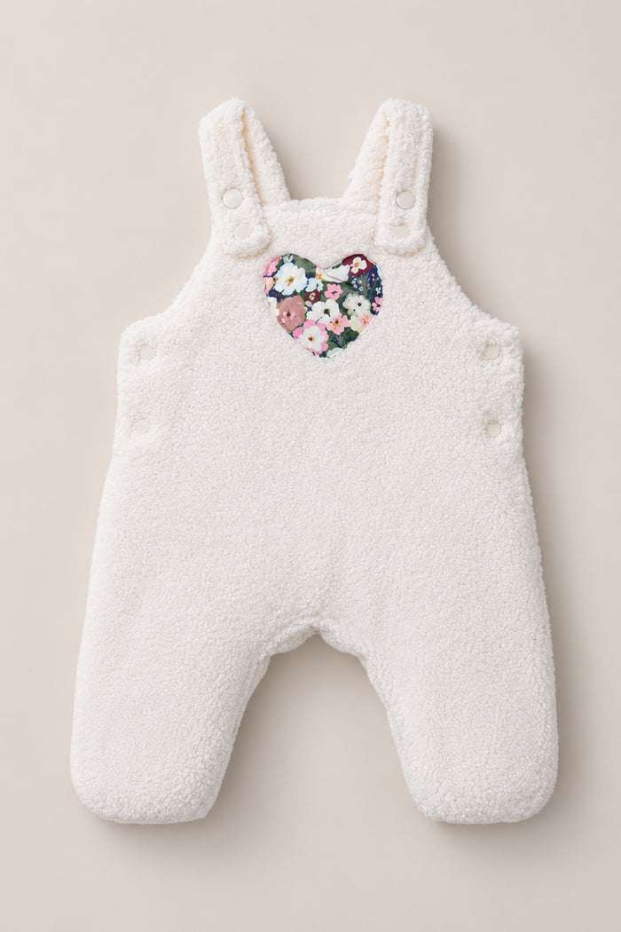 The Baby Siena Onesie in Ivory & Midnight Garden by Ivy City Co is a white fleece baby romper with shoulder straps and side buttons, adorned with a heart-shaped floral patch on the chest—an irresistibly cozy sleeveless piece that will keep your little one warm and stylish.