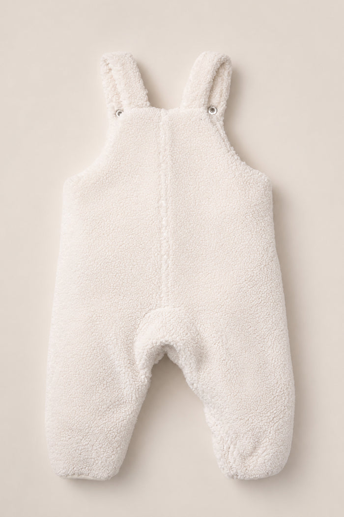 The Baby Siena Onesie in Ivory & Midnight Garden by Ivy City Co is a white, fuzzy sherpa romper with shoulder straps and convenient snap closures, shown laid flat on a neutral background. This sleeveless design features soft, warm fabric to keep babies cozy during chilly weather.