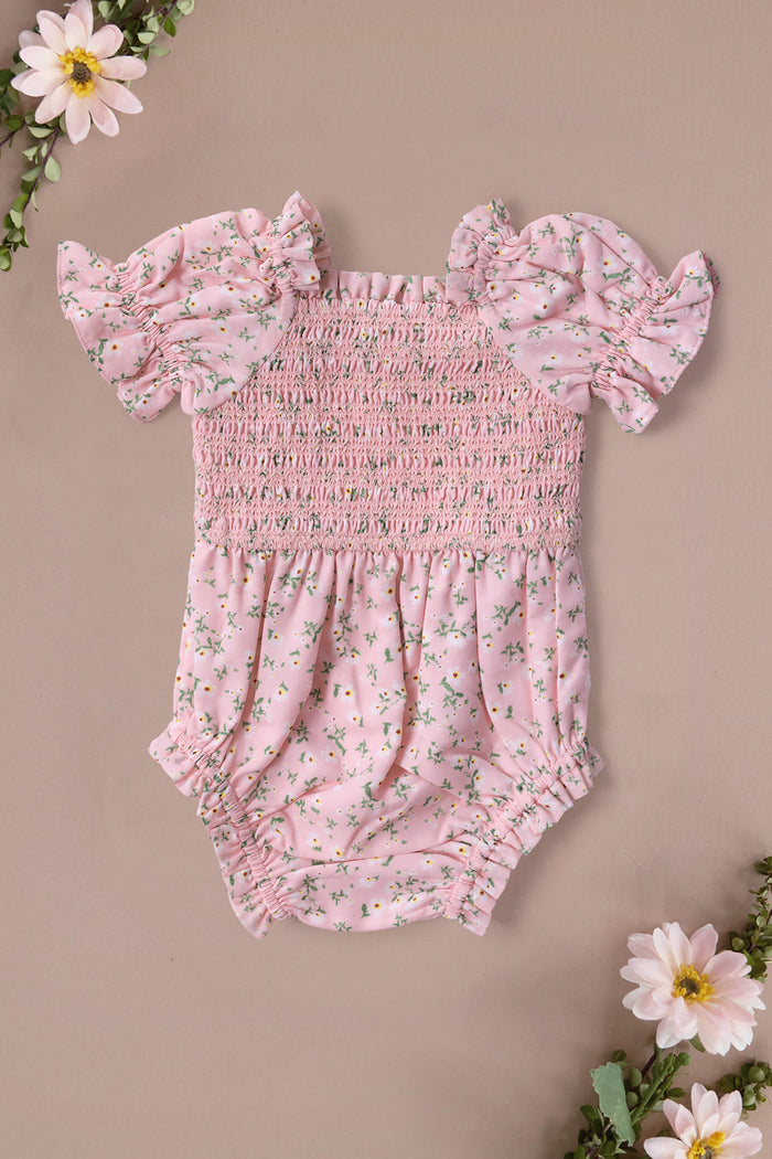 The Ivy City Co Baby Valencia Romper in Pink Ditsy Floral features a smocked bodice and short ruffled sleeves, showcased on a beige background with decorative corner flowers.