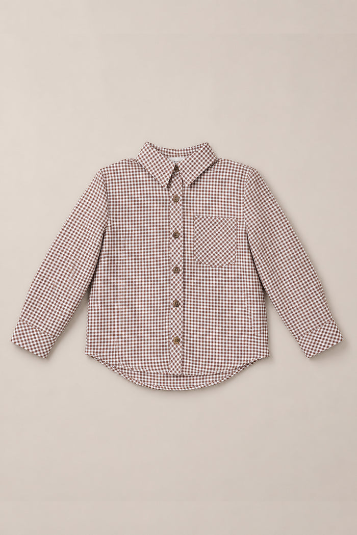 The Ivy City Co Boys John Shirt in Brown Gingham is a long-sleeve, button-up children’s shirt featuring a brown gingham pattern, single chest pocket, and a pointed collar. Crafted from soft woven cotton, the shirt is shown laid flat on a neutral background.