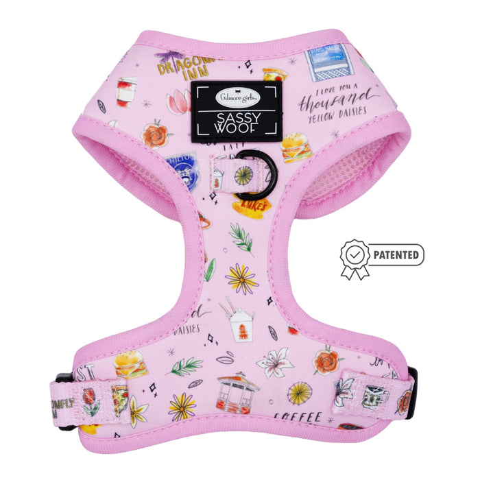 The Dog Adjustable Harness - Gilmore Girls™ by Sassy Woof showcases colorful Stars Hollow-inspired icons like flowers, food, drinks, and travel motifs. Features a Sassy Woof label and patented design symbol on the front.