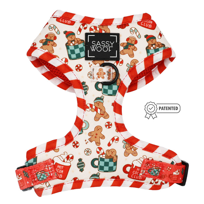The Sassy Woof Dog Adjustable Harness - Hot Cocoa Club features festive red and white stripes, gingerbread cookies, candy canes, mugs, and branding on a cream background. Includes a Patented badge on the right.