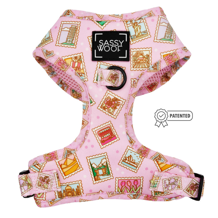 The Sassy Woof Dog Adjustable Harness - Out of Office is a pink, no-pull harness featuring postage stamp landmark prints, black hardware, adjustable straps, and a front Sassy Woof label. A Patented icon appears beside it.