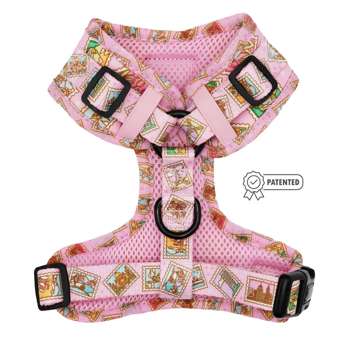 The Sassy Woof "Dog Adjustable Harness - Out of Office" is a pink harness with colorful postage stamp patterns, black buckles, and a patented design label.