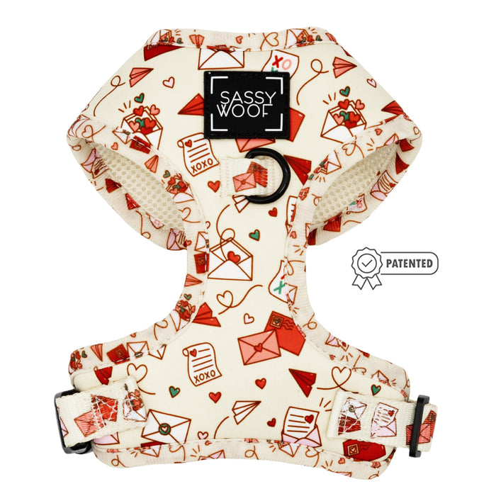The Sassy Woof Dog Adjustable Harness - P.S. I Woof You is cream-colored with a Valentine's Day theme, featuring red and pink love letters, paper airplanes, hearts, XOXO text, a Sassy Woof label, and a patented symbol.