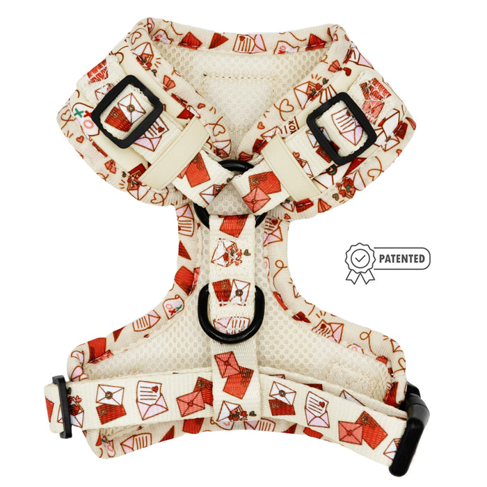 The Sassy Woof Dog Adjustable Harness - P.S. I Woof You features a cream base with red and pink envelope patterns, black plastic buckles, metal rings, and a PATENTED badge icon—a stylish pick for dog accessories.