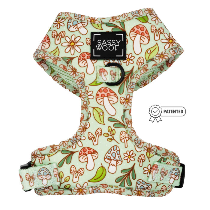 The Sassy Woof Dog Adjustable Harness - Shrooms & Blooms is green with red and white mushroom and flower prints, adjustable straps, a black brand logo patch, metal leash ring, and a patented badge graphic on the side.
