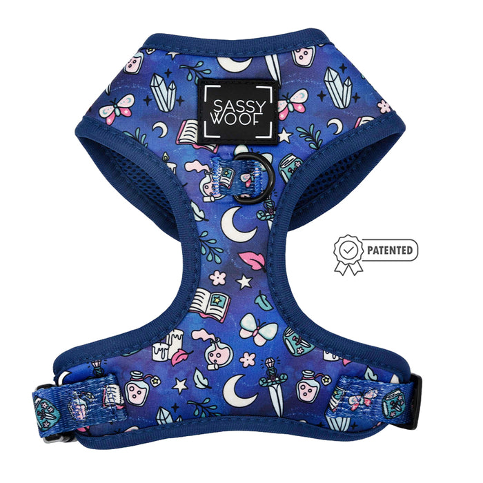 The Sassy Woof Spellbound Dog Adjustable Harness features a magical blue pattern with books, moons, stars, crystals, swords, and plants. It has a black logo patch at the top center and includes a patented icon.