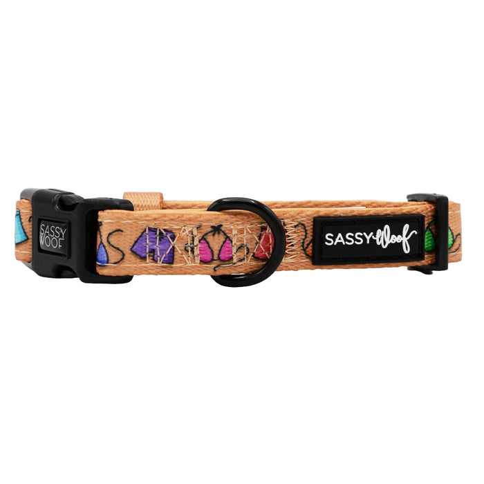 The Sassy Woof Dog Collar - Beach Bod is a tan, adjustable neoprene collar with tropical fruit designs, black plastic buckle, metal D-ring, and a white “Sassy Woof” logo on a black patch—ideal for your growing pup.