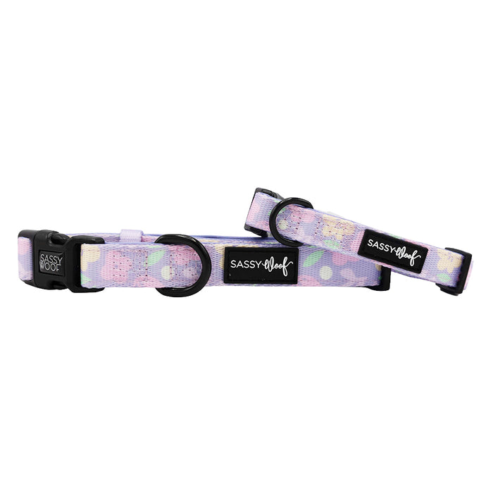 Two Sassy Woof "Fleur de Sass" pastel purple adjustable dog collars, each with abstract patterns, black buckles, sturdy metal rings, and a branded label for comfort and style.