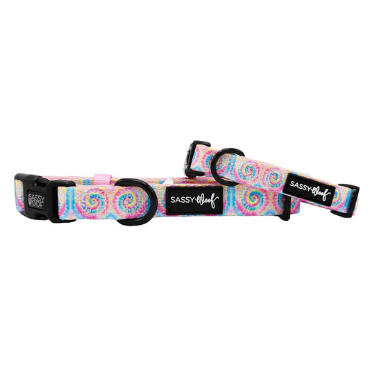 Two Sassy Woof "Good Vibes" adjustable dog collars with pastel pink, blue, and yellow tie-dye, black plastic buckles, metal loops, and a Sassy Woof logo tag.