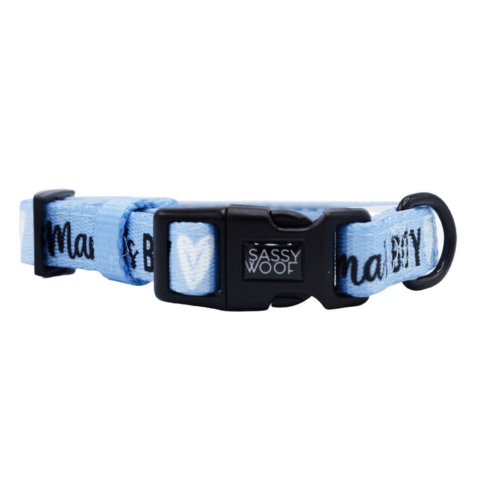 The Sassy Woof Dog Collar - Mama's Boy is a light blue adjustable neoprene collar with a black plastic buckle, white heart designs, and "MAMA’S BOY" printed on the fabric.