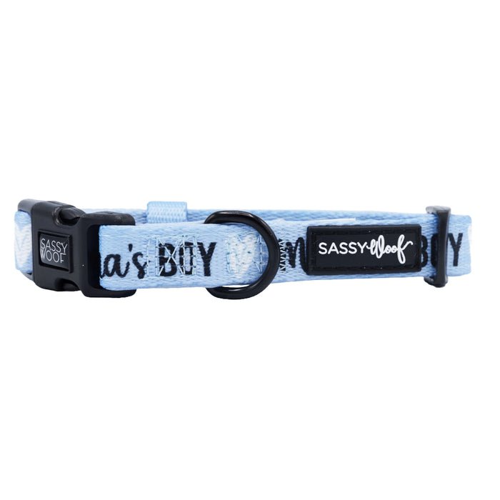 The Sassy Woof Dog Collar - Mama's Boy is a light blue neoprene collar with an adjustable fit, black plastic buckle, metal ring, and repeating "MAMAS BOY" text—ideal for pups on the Puppy Growth Pawtection Plan.