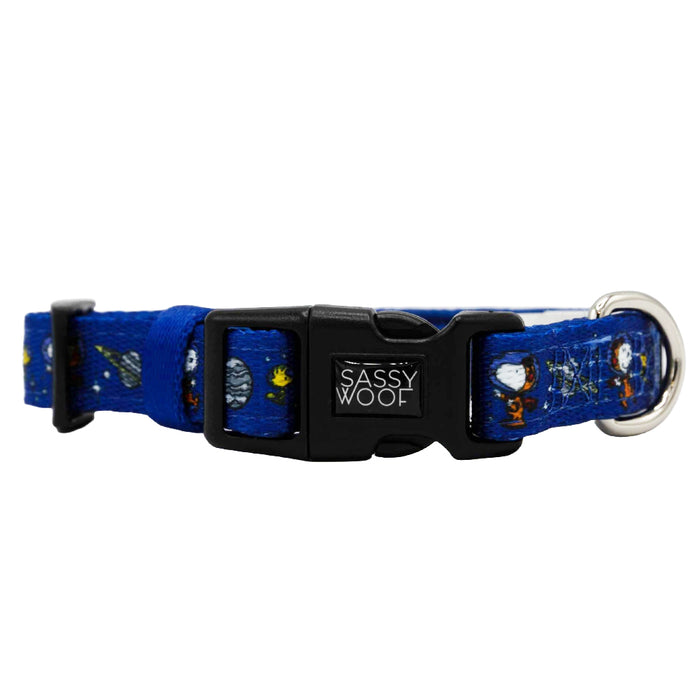 The Sassy Woof Dog Collar - Peanuts™ Snoopy in Space features a blue, space-themed design with planets and astronauts, a black Sassy Woof buckle, and a metallic D-ring for leash attachment.