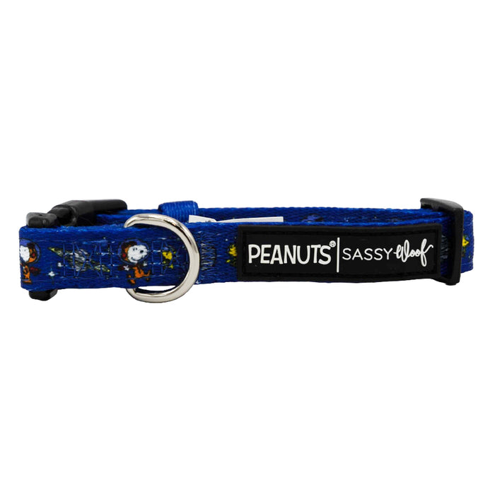 The Dog Collar - Peanuts™ Snoopy in Space by Sassy Woof is a blue adjustable collar with Peanuts characters, a plastic buckle, metal D-ring, and a black patch reading PEANUTS | SASSY WOOF—perfect for Peanuts fans.