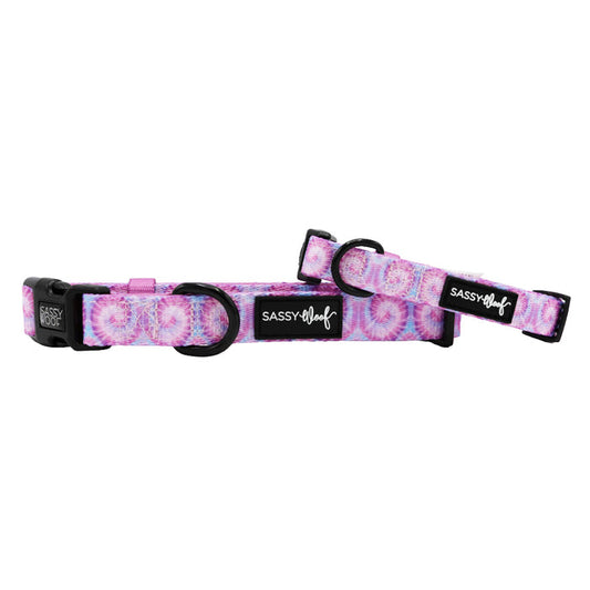 Two Sassy Woof "Purple Haze" tie-dye dog collars feature black plastic buckles, metal rings, and a black Sassy Woof logo tag—perfect adjustable collars to suit your puppy's growth.