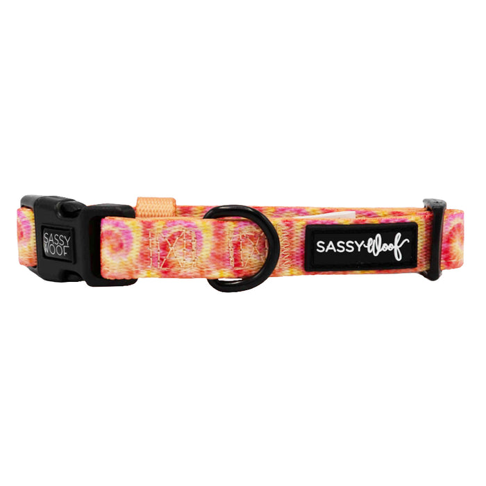 The Sassy Woof Dog Collar - Summer Sorbet features a pink, orange, and yellow tie-dye print with a black buckle, metal ring, and logo patch—an adjustable fit perfect for your puppy's growth.