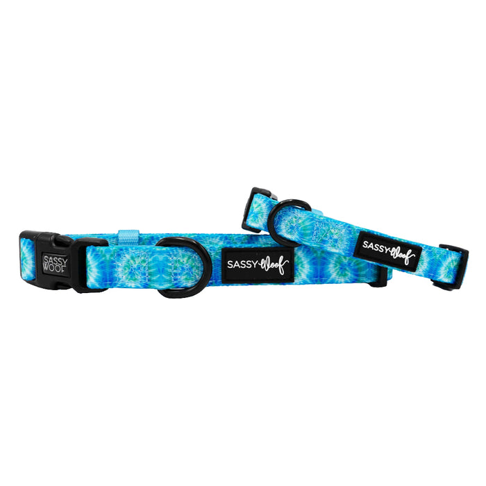 Two Sassy Woof "Dog Collar - Tropical Tides" blue adjustable collars with a vibrant tie-dye pattern, soft neoprene, black plastic buckles, and Sassy Woof logo tags are shown on a white background.