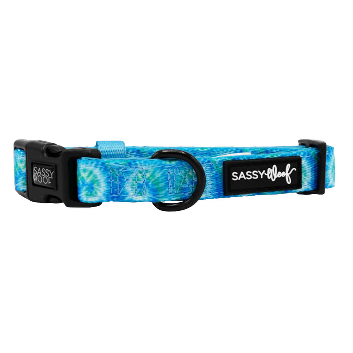 The Sassy Woof Dog Collar - Tropical Tides features a blue tie-dye design, black buckle, metal D-ring, and side brand label. This adjustable collar offers your pup a secure and comfortable fit.
