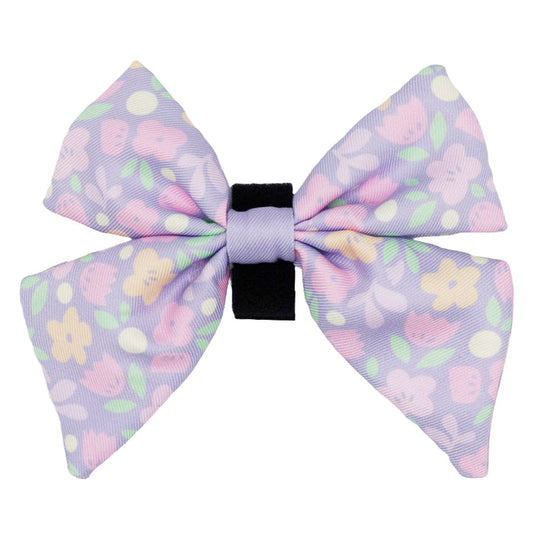 Add charm to any dog collar or harness with the Sassy Woof Dog Sailor Bow - Fleur de Sass, a pastel purple bow featuring pink, yellow, and green floral patterns with a black center band.