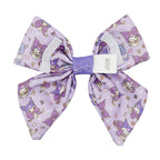 The Dog Sailor Bow - Kuromi™ by Sassy Woof features a large lavender design with cute cartoon cats in purple hats and dresses, hearts, and flowers. A white center label displays the brand—perfect for pairing with any stylish dog collar.