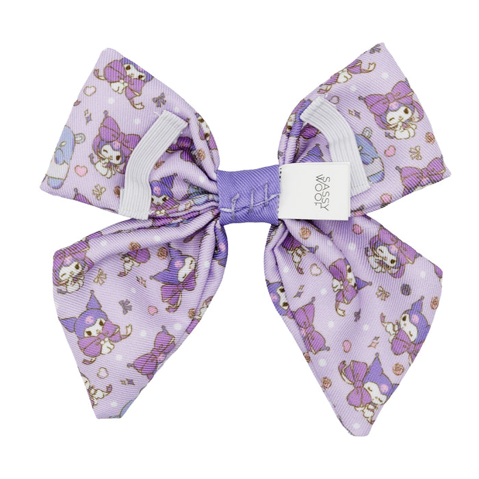 The Dog Sailor Bow - Kuromi™ by Sassy Woof features a large lavender design with cute cartoon cats in purple hats and dresses, hearts, and flowers. A white center label displays the brand—perfect for pairing with any stylish dog collar.