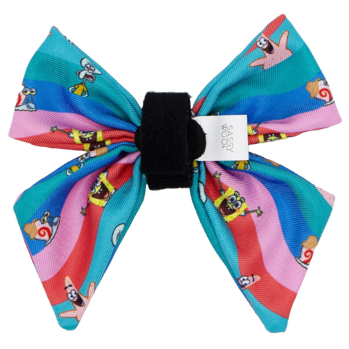 The Sassy Woof Dog Sailor Bow - SpongeBob SquarePants™ and Friends features wavy red, pink, blue, and teal stripes with SpongeBob characters, a black center, and a white tag—ideal to pair with other SpongeBob pet gear.