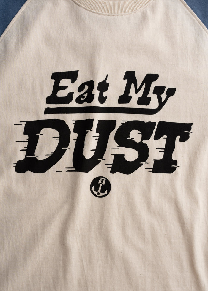 Beige shirt with bold black text "Eat My Dust" and a small anchor symbol below, creating a casual, playful statement.