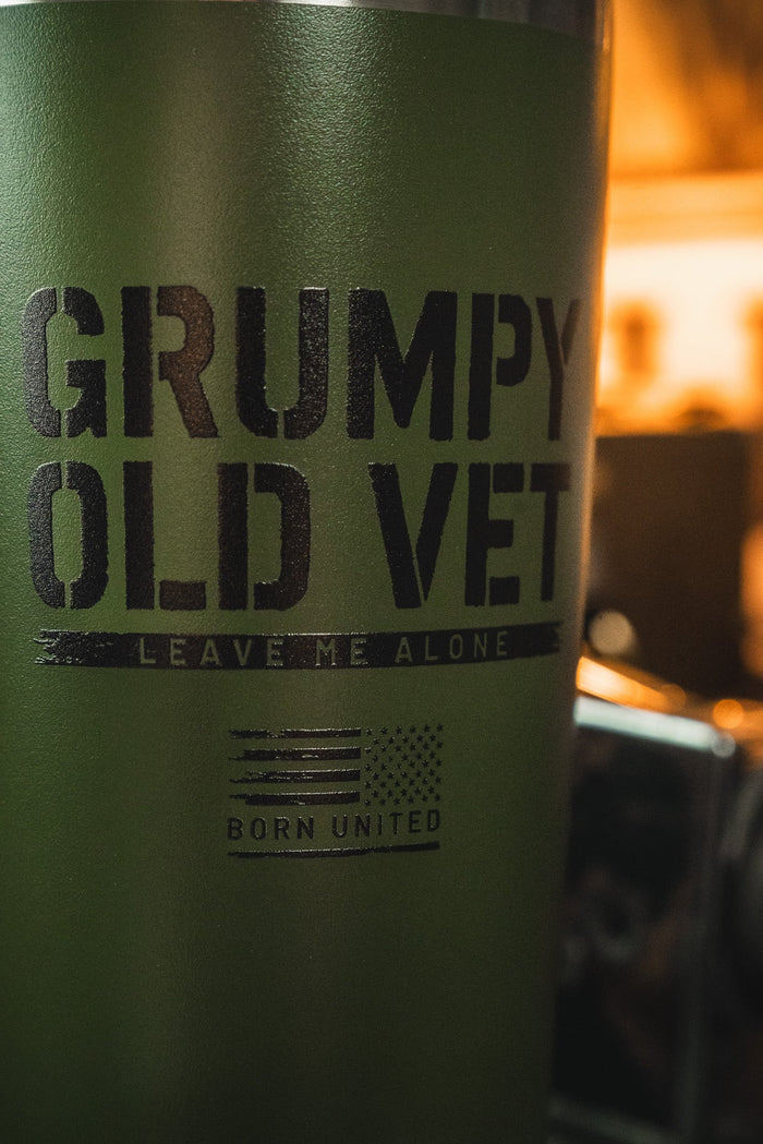 The Grumpy Old Vet Tumbler - 20oz by Born United Private Label is a green stainless steel tumbler with black "GRUMPY OLD VET - LEAVE ME ALONE" text, a small American flag, and "BORN UNITED." It keeps drinks hot or cold on the go.