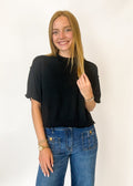 Woman wearing a black top and blue jeans against a white background