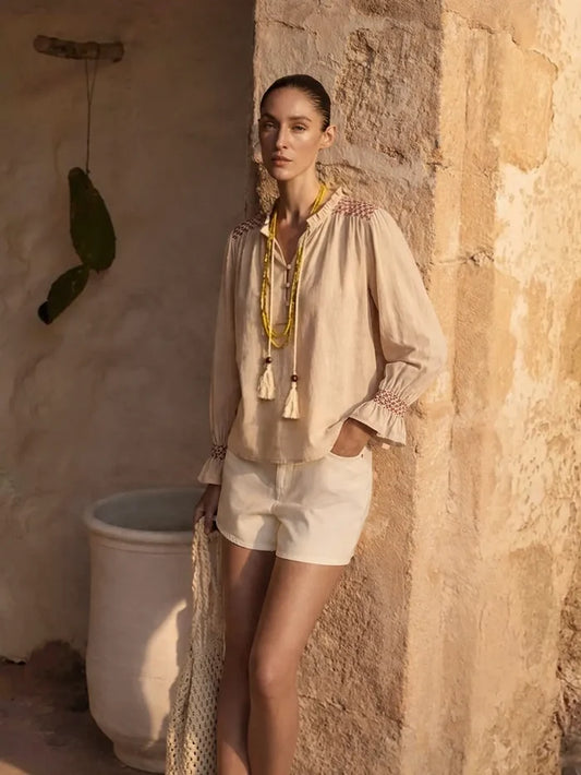 Woman in a beige outfit standing against a textured wall with a cactus plant.