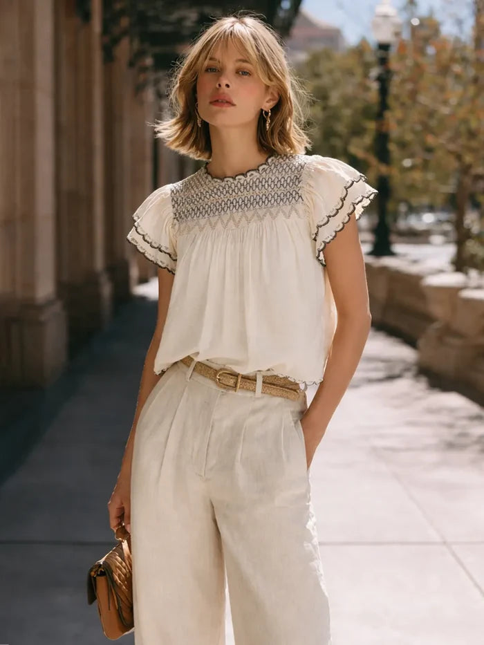 Woman wearing a white blouse with lace details and beige pants on a city street.