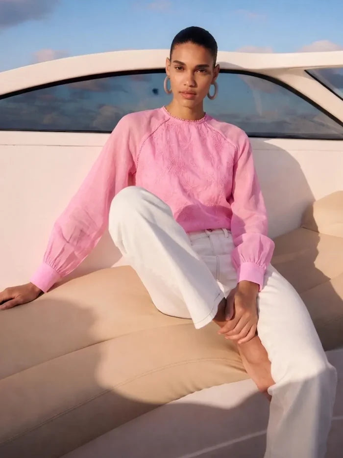 Person wearing a pink sweater and white pants sitting on a boat.