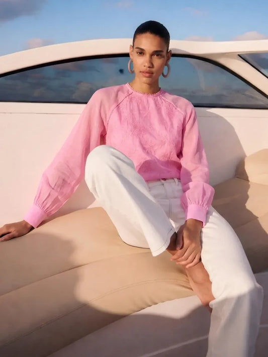 Person wearing a pink sweater and white pants sitting on a boat.