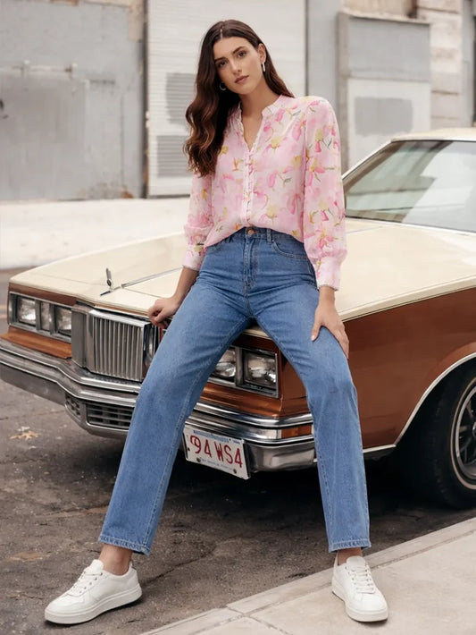 Woman in a floral blouse and jeans leaning against a vintage car.