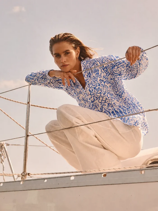 Woman in a blue patterned shirt and beige pants on a boat with a clear sky background
