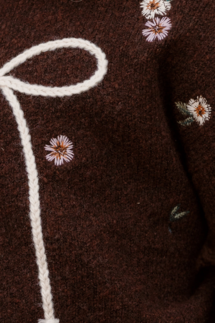 Close-up of brown knit fabric with small embroidered flowers and a white braided cord tied in a loop, highlighting the charming embroidered details of the Ivy City Co Mini Ellis Sweater in Warm Cocoa Lovelorn Ditsy.