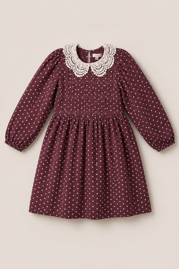 The Mini Jillian Dress in Aubergine Ditsy Dot by Ivy City Co is a long-sleeved dress adorned with white polka dots, crafted from soft viscose fabric, and featuring delicate puff sleeves, a smocked bodice, gathered skirt, and a decorative white lace collar. The dress is displayed on a light background.