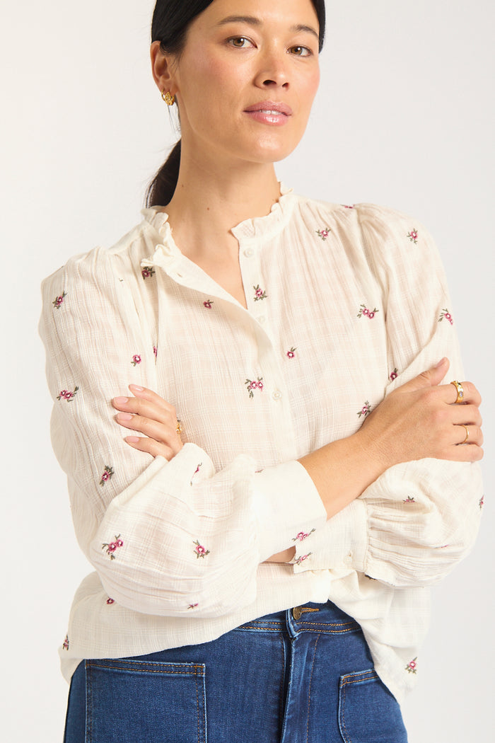 Woman against white background in cream shirt with mauve flowers.
