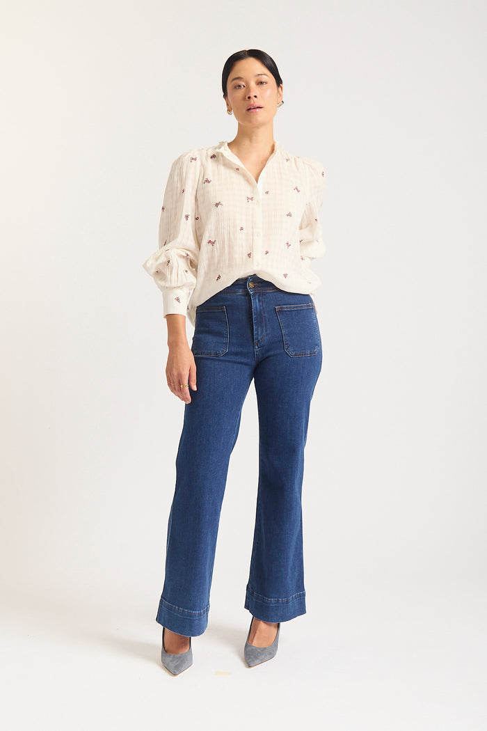 Woman against white background in cream shirt with mauve flowers.