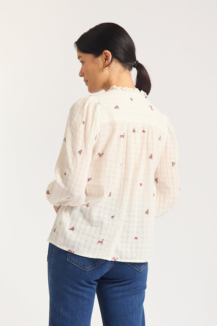 Back of a oman against white background in cream shirt with mauve flowers.