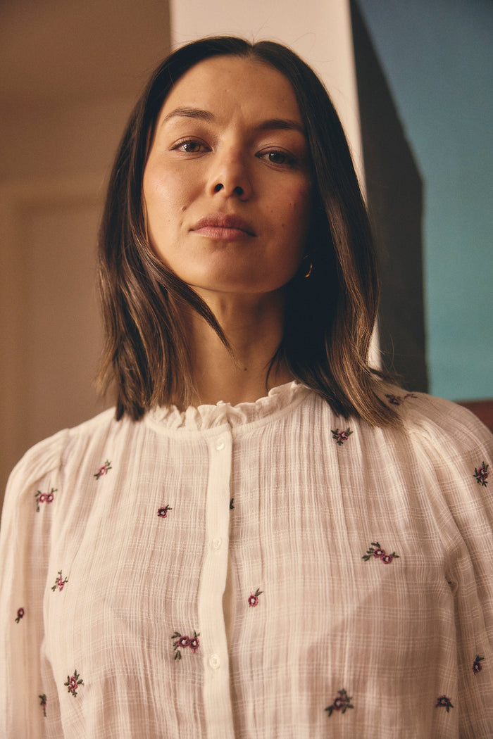 Woman against in front of artwork,  in cream shirt with mauve flowers.