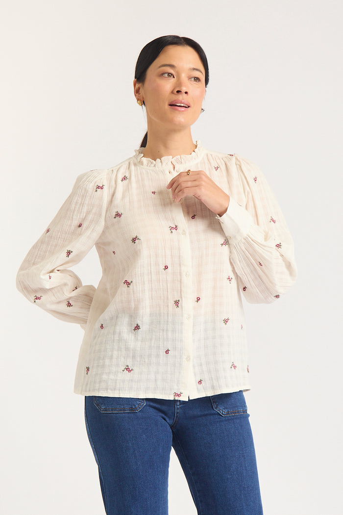 Woman against white background in cream shirt with mauve flowers.