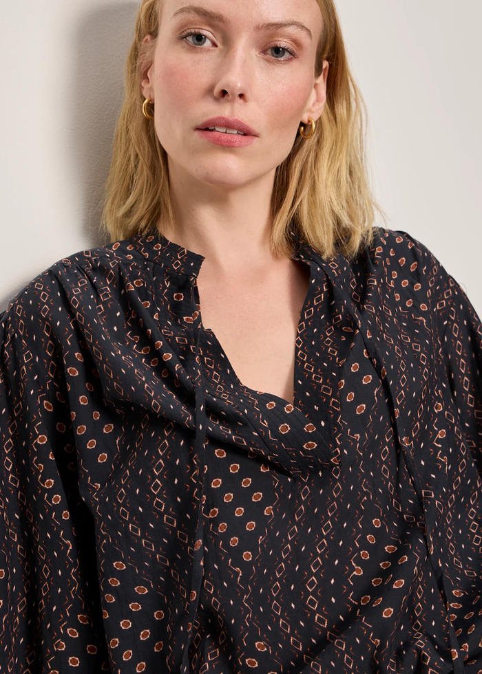 Woman wearing a black and brown patterned blouse with white shorts