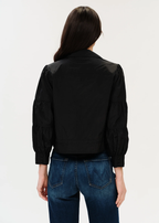 Woman with dark hair posing in black jacket turned around.